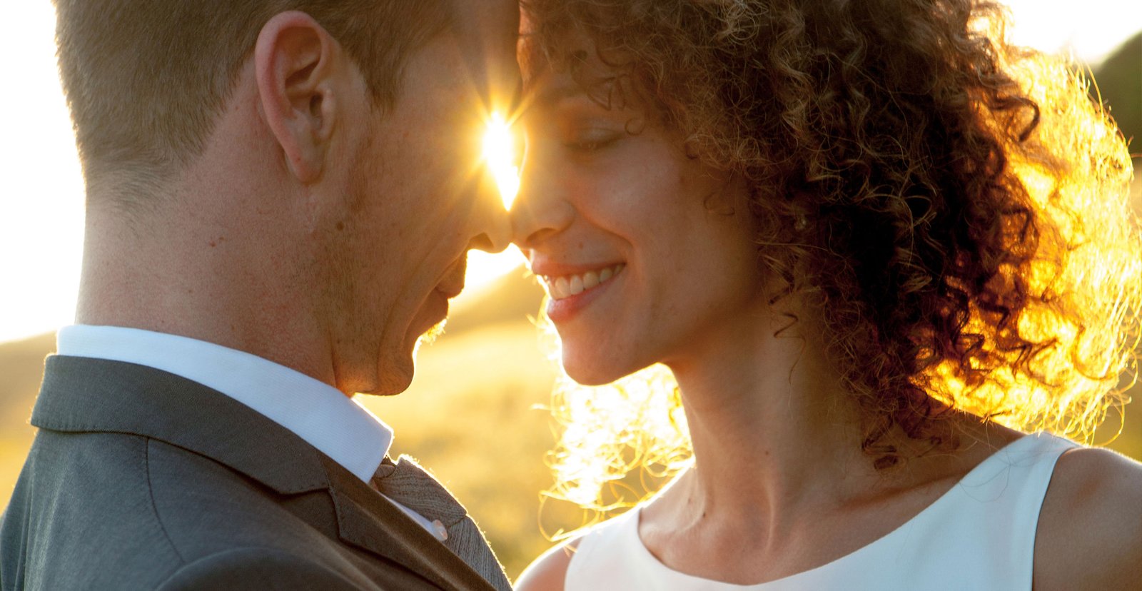 The bride and groom touch foreheads, feeling each other's closeness as sunlight shines through.