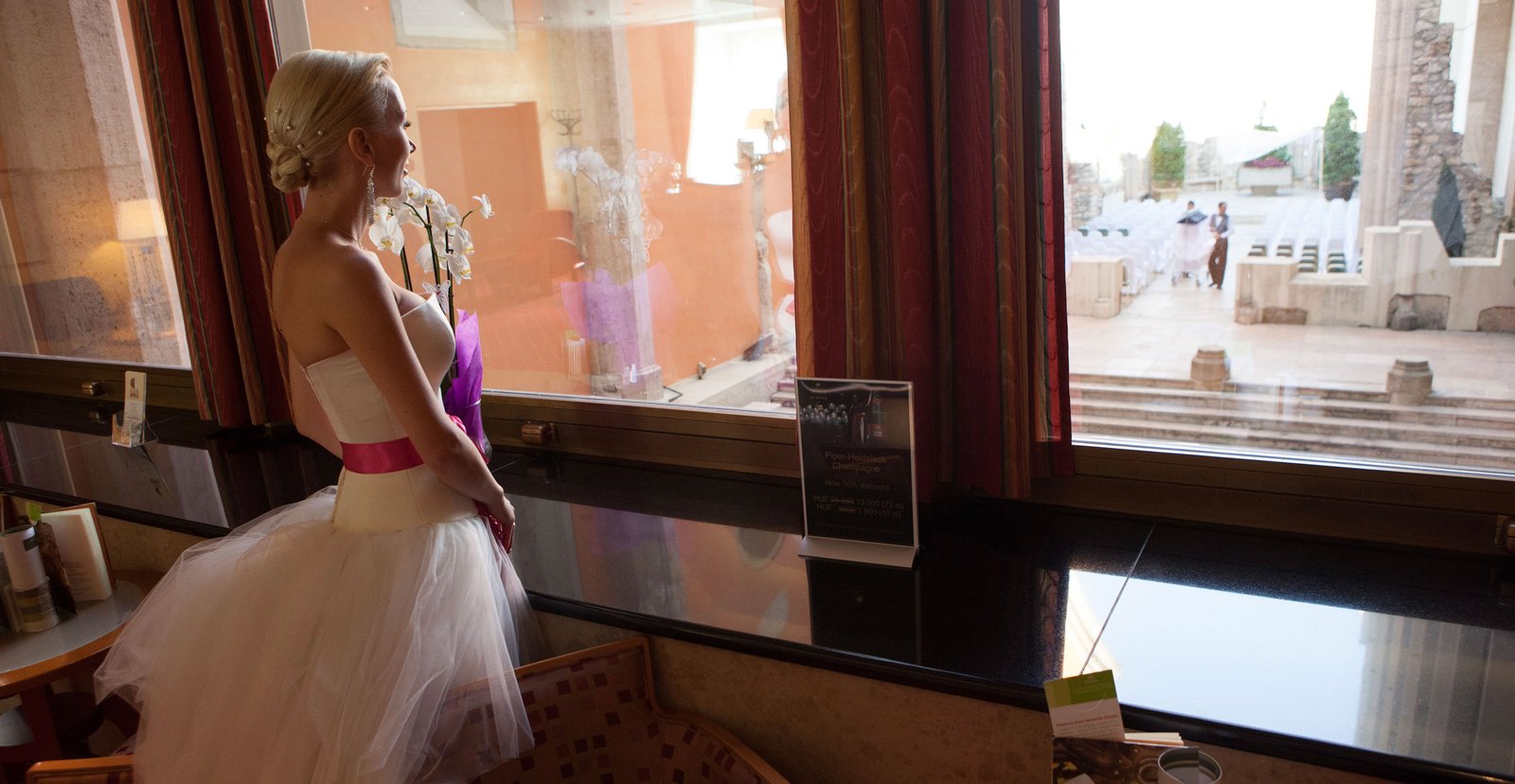 The bride looks out the window at the ceremony venue where her wedding will soon take place.
