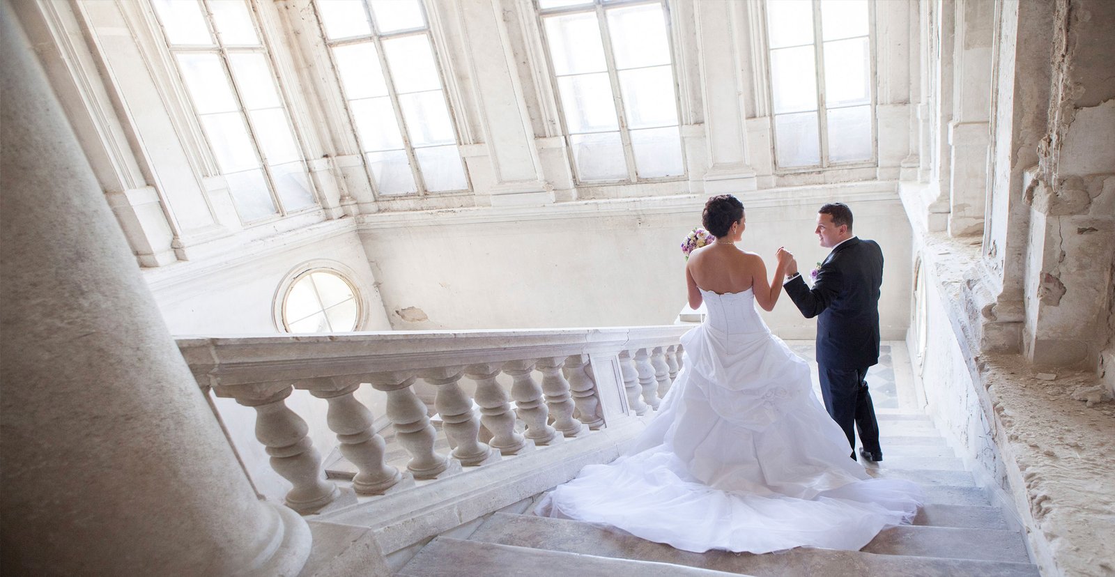The bride and groom are posing on a grand staircase in an abandoned castle, with the bride walking like a princess.