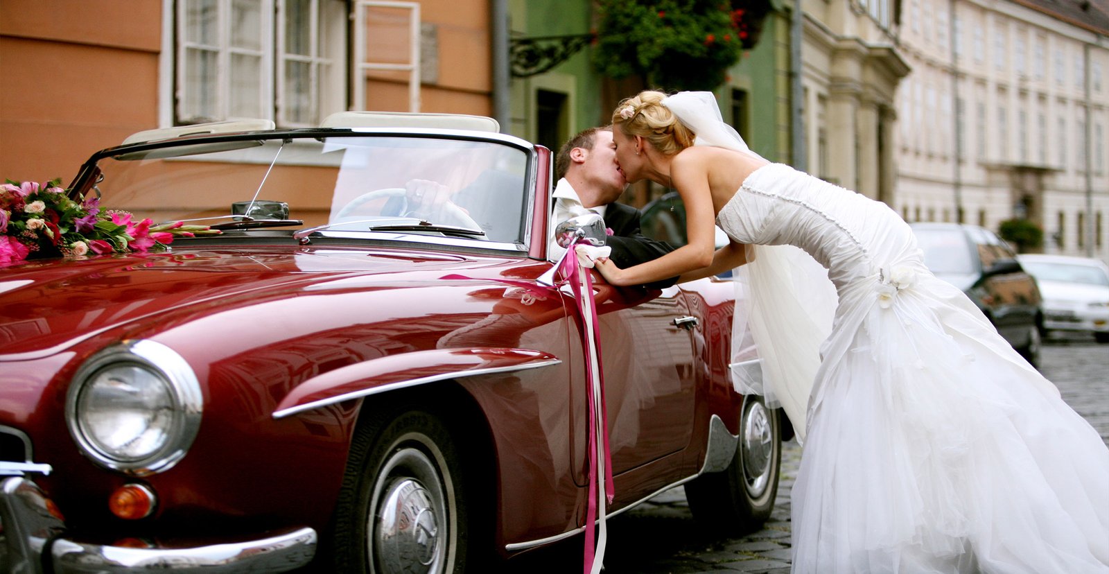 The bride and groom kiss next to a beautiful vintage fire-red Mercedes cabriolet.